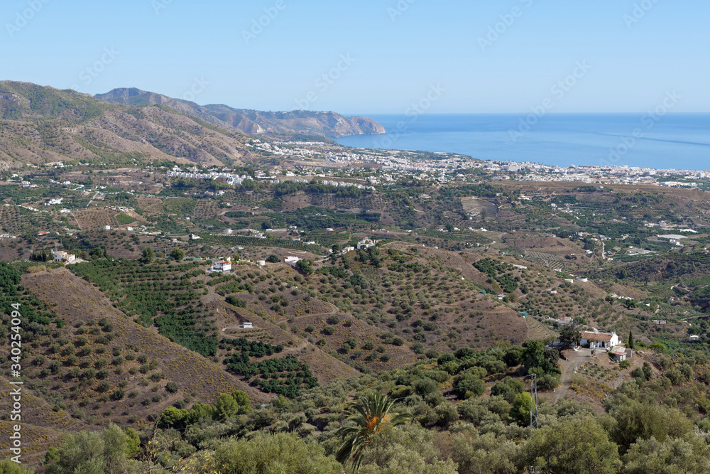 View from the white village of Frigiliana over the beautiful green and cultivated hilly landscape down to the city of Nerja and the sea; Spain, Europe
