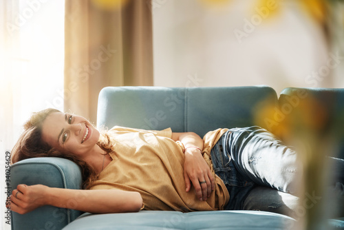 Happy young beautiful charming woman girl lying on a sofa in her living room at home, charmingly smiling and looking at the camera