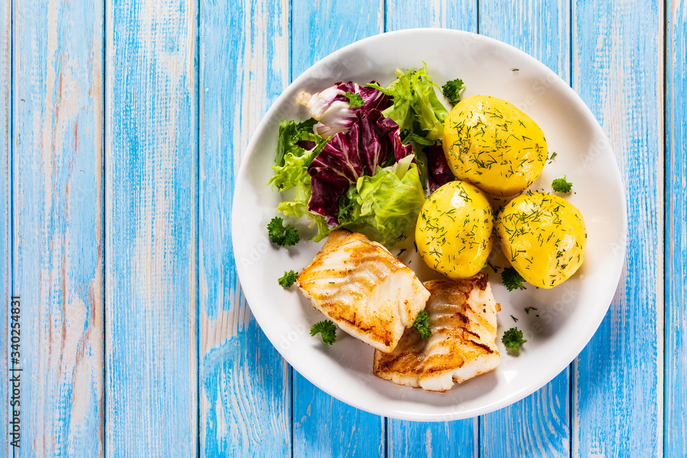 Fish dish - fried cod fillet with potatoes and vegetables on wooden table
Fish dish - fried cod fillet with potatoes and vegetables on wooden table