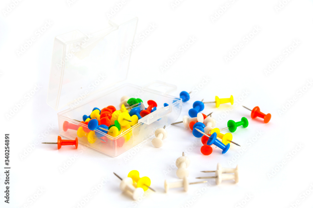 Plastic box with multi-colored pushpins over on the white background. Some of the pins scattered around.