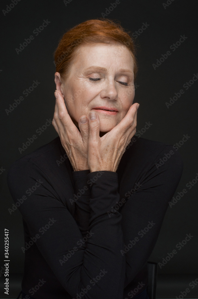 Red-haired elderly lady in a black sweater on a dark gray background Red-haired elderly lady in a black sweater on a dark gray background