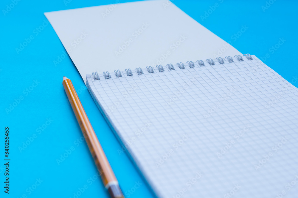 An opened caged notebook with pencil over turquoise background. Selective focus. An opened caged notebook with pencil over turquoise background. Selective focus.