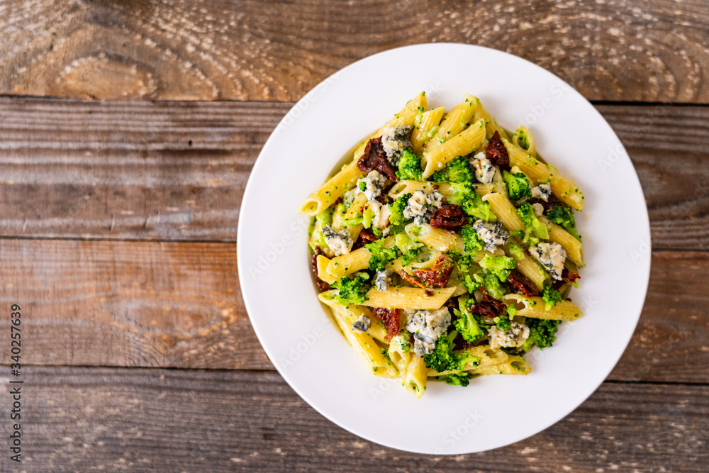 Penne with gorgonzola broccoli and sun-dried tomatoes on wooden table Penne with gorgonzola broccoli and sun-dried tomatoes on wooden table
