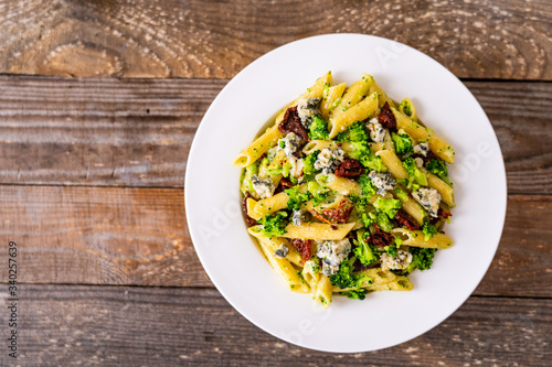 Penne with gorgonzola broccoli and sun-dried tomatoes on wooden table