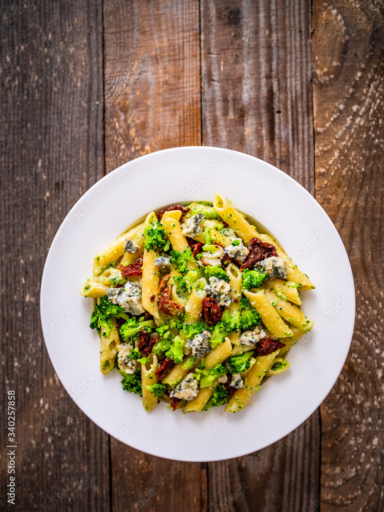 Penne with gorgonzola broccoli and sun-dried tomatoes on wooden table