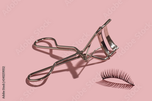 Fotografija A metal lash curler with false lashes composition on pink background