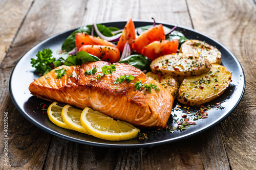 Fried salmon steak with potatoes and vegetables on wooden table