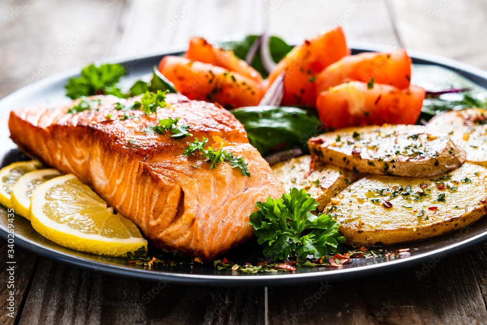 Fried salmon steak with potatoes and vegetables on wooden table Fried salmon steak with potatoes and vegetables on wooden table