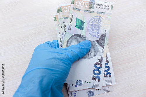 Hand in blue glove holding money 500 hryvnia banknotes on a white background. Concept of dirty money close up on the center