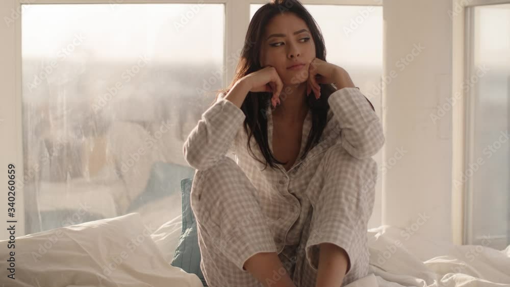 Asian Woman Sitting on a Bed at Home Asian Woman Sitting on a Bed at Home