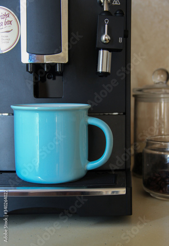 Blue coffee mug and coffee machine standing in the kitchen. Professional coffee blending machine.