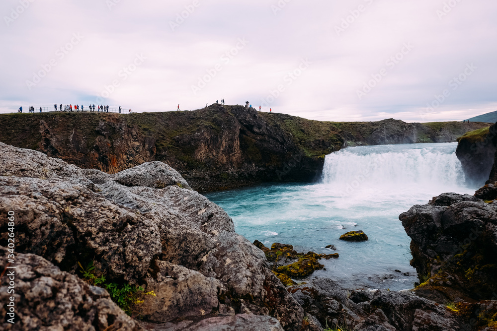view of the river and crowds of tourists near a waterfall in Iceland near Lake Myvatn in summer on a cloudy day