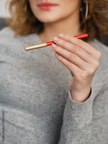 Woman s beauty blogger hands holding red cosmetic pencil with blurred body background  warm cozy tones and copyspace