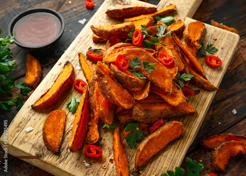 Healthy Baked Orange Sweet Potato wedges with dip sauce, herbs, salt and pepper on wooden board © grinchh