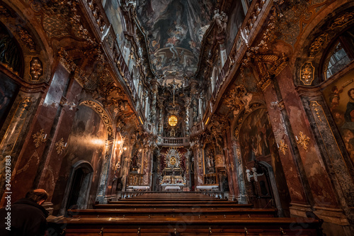 Prayer in Late Baroque church Asamkirche with lights on before sunset in Munich, Germany