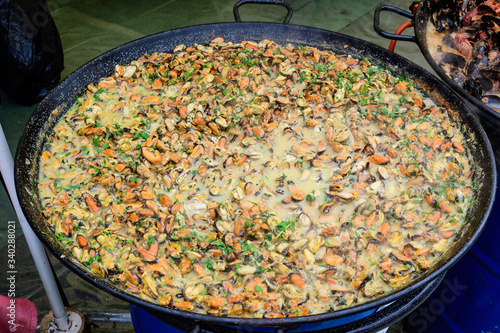 Large group of cooked mussels with tomato and cream sauce at a street food festival, ready to eat seafood,  beautiful orange monochrome outdoor background
