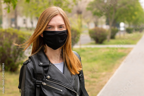 Woman wearing face mask during coronavirus outbreak. Redhead girl in a black face mask on a street.