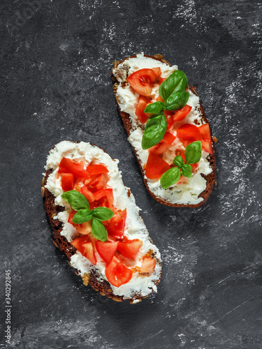 Traditional Italian snack. Bruschetta caprese toast with tomatoes, soft cottage cheese and basil on a dark black background. Top view. Copy space