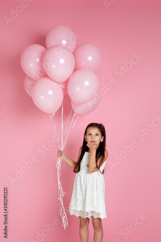 Smiling adorable little child girl with pastel pink air balloons sends a kiss isolated over pink background. birthday party. copy space