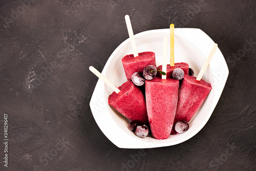 frozen red ice cream on a stick with chunks of ice and cherries in a white plate on a black background. cherry strawberry watermelon ice cream with dry ice on the table
