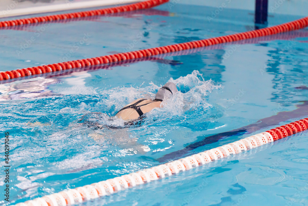 Swimming pool athlete training indoors for professional competition. Female swimmer performing the butterfly stroke at indoor swimming competition