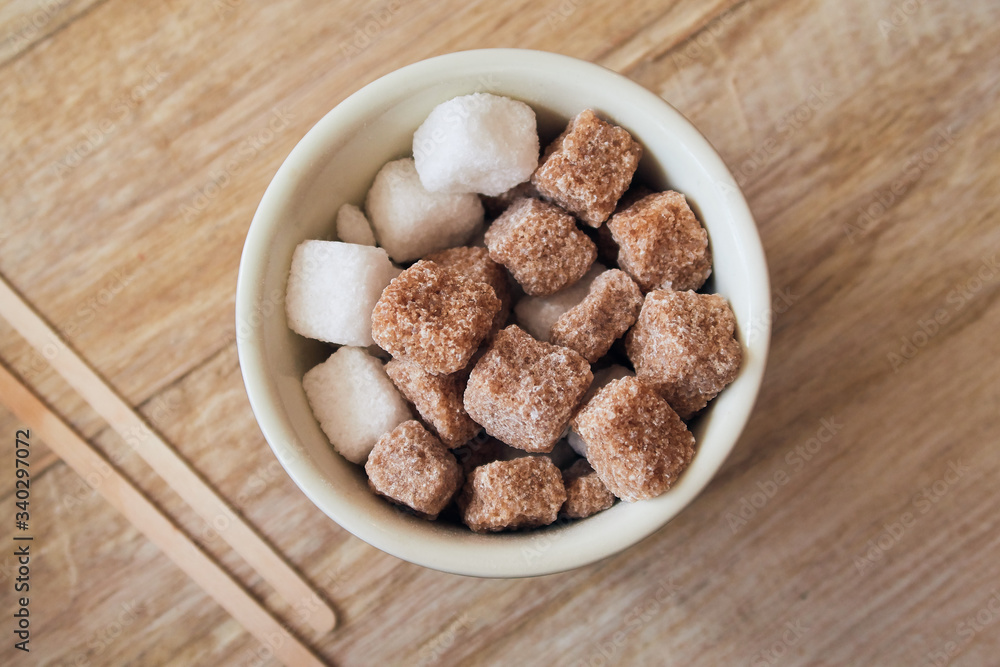 Abowl of brown crystallised sugar cubes from above, in a hipster coffee shop on a rustic brown table, photographed with a shallow depth of field. Sugar cubes perfect for tea and coffee hot drinks. Abowl of brown crystallised sugar cubes from above, in a hipster coffee shop on a rustic brown table, photographed with a shallow depth of field. Sugar cubes perfect for tea and coffee hot drinks.