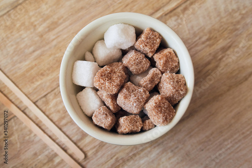 Abowl of brown crystallised sugar cubes from above, in a hipster coffee shop on a rustic brown table, photographed with a shallow depth of field. Sugar cubes perfect for tea and coffee hot drinks.