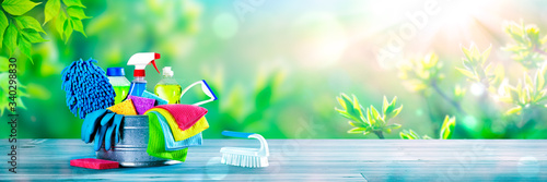 Bucket Of Cleaning Supplies On Wooden Table With Fresh Spring Background - Cleaning Services Concept