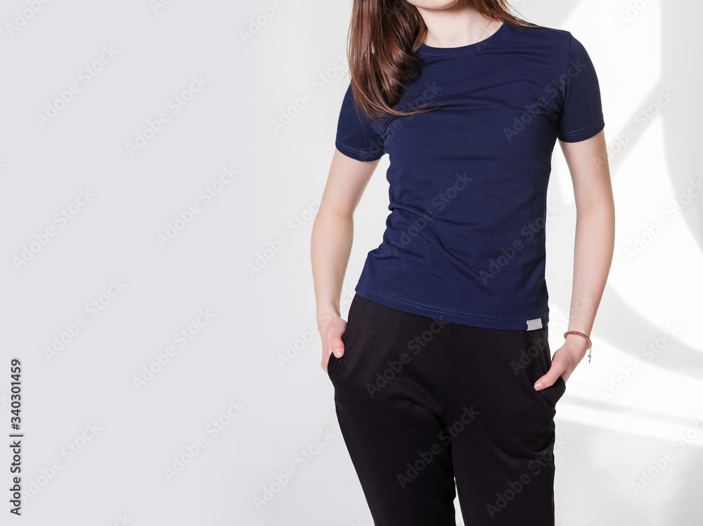 Young girl wearing blank t-shirt and and sport pants. Gray wall background shadow light from the window with copy space for your text message or promotional content Young girl wearing blank t-shirt and and sport pants. Gray wall background shadow light from the window with copy space for your text message or promotional content