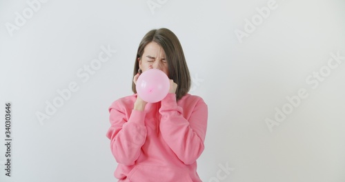 Young woman blowing a pink balloon