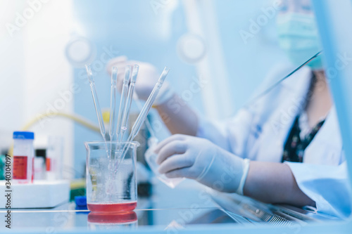 dropper pipette in beaker and scientist using dropper pipette transfer sample in Biosafety cabinet on background. select focus on beaker