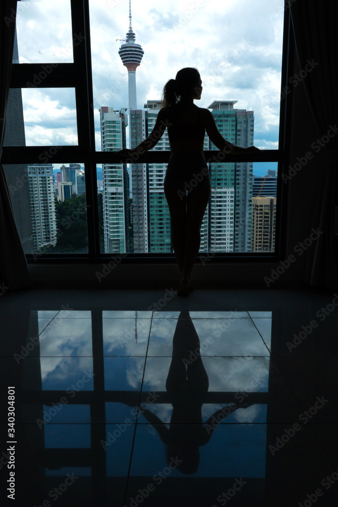 Fototapeta premium A slender girl is looking at the city through a large window. High floor.