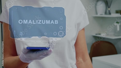 Doctor in medical glove against background of doctor's office with HUD hologram text Omalizumab. Hand holds futuristic holographic gadget. Medical technology concept of the future photo