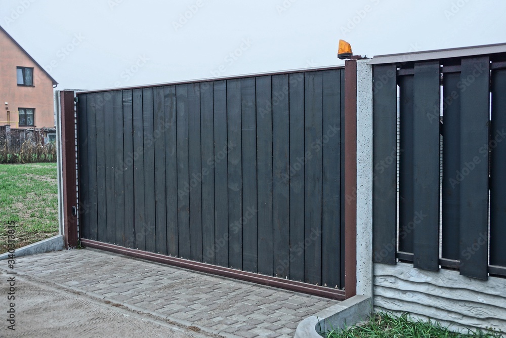 gray black private gate and wooden plank fence on a rural street - obrazy, fototapety, plakaty 