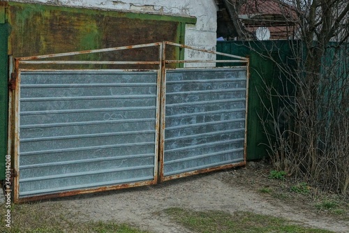 Fototapeta Naklejka Na Ścianę i Meble -  old gray metal gate and part of a green fence on a rural street