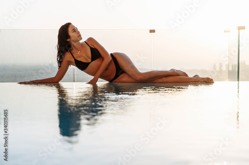 Emotional portrait of Fashion stylish pretty young woman, soft colors. Sunset city background. Girl lies and relaxes on the edge of the infinity pool