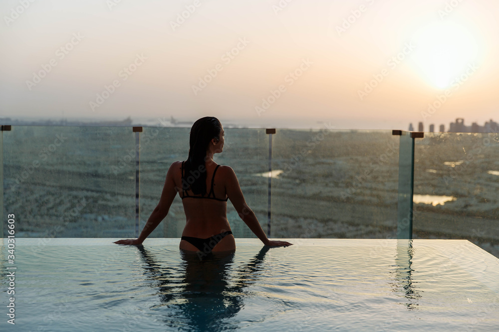 Woman relaxing in infinity pool with sunset city view. Relaxing vacation.  Dubai UAE