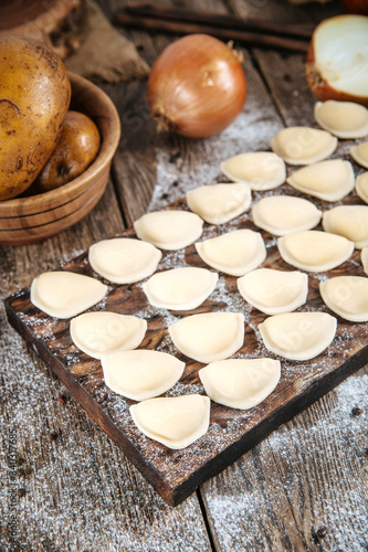Raw uncooked semi-finished small vareniki dumplings with a filling on a wooden board on a table, vertical format