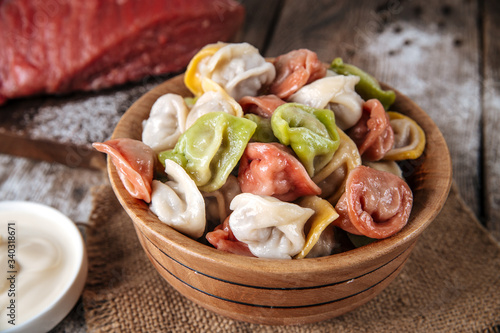 Closeup on raw semi-finished multi-colored dumplings in a bowl on the wooden table with sour cream, horizontal