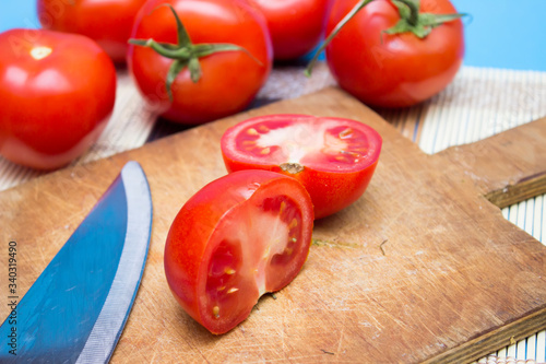 Fresh, red tomatoes on a cutting board with a blue background up close
