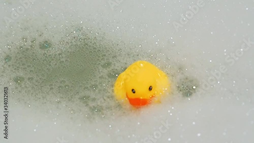 rubber yellow duck toy floats in water in bath with foam
