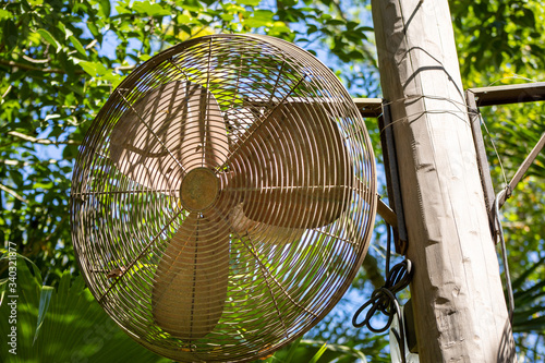 A rusted oscillating fan high on a post on a sunny day