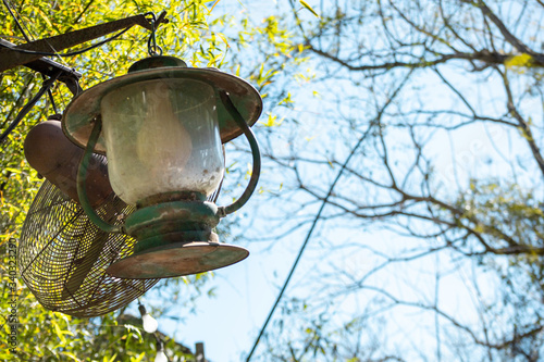 A rustic lantern hanging in the sunlight with trees in the background