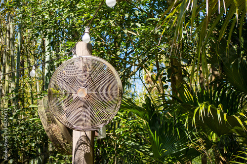 A rusted oscillating fan high on a post on a sunny day
