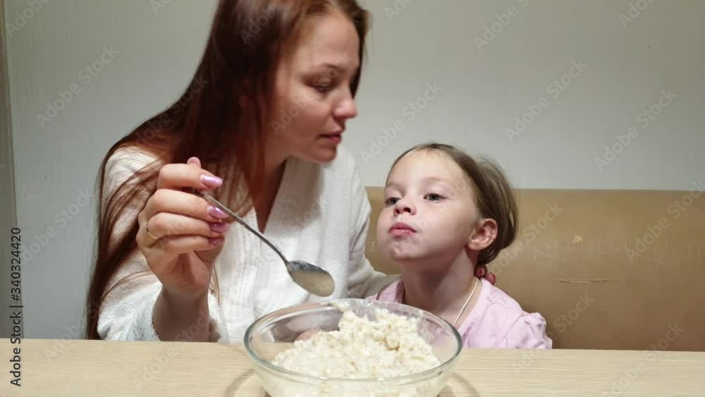 a woman feeds a little girl oatmeal for dinner in the kitchen.