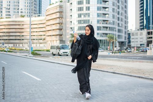 Beautiful Arab woman in abaya with water bottle and sport's bag going to a gym