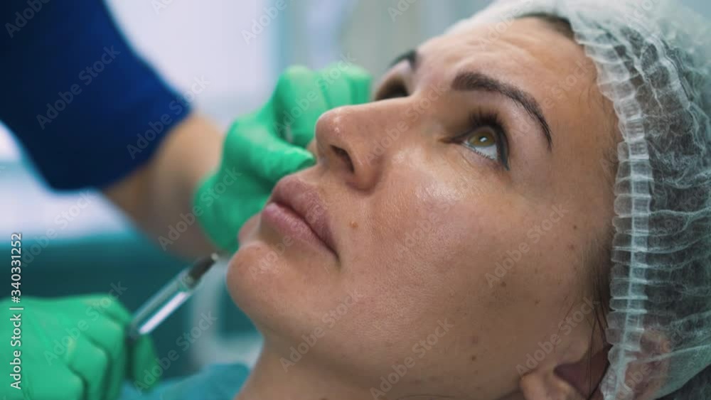 CU shot: pretty woman undergoes procedure of anti-aging facial filler injection on cheek with cosmetologist in modern beauty clinic closeup CU shot: pretty woman undergoes procedure of anti-aging facial filler injection on cheek with cosmetologist in modern beauty clinic closeup