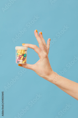 Close-up of female hand holding bottle with capsules and pills over blue background