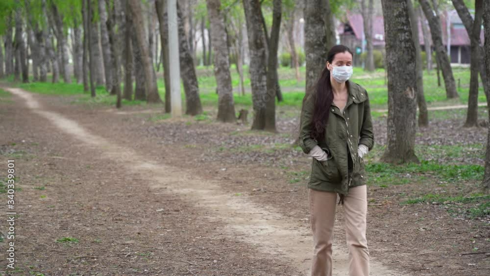 Wonderful cute Russian woman in protective medical face mask with long brown hair walks alone in summer forest, enjoys nature and fresh air, looks up on the sun at the sky outdoor. Isolation concept. Wonderful cute Russian woman in protective medical face mask with long brown hair walks alone in summer forest, enjoys nature and fresh air, looks up on the sun at the sky outdoor. Isolation concept.