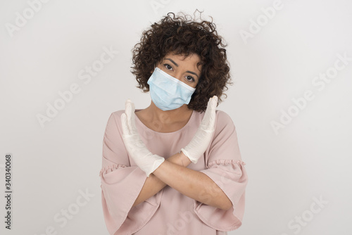 Young beautiful brunette girl wearing medical mask standing over isolated background. Has rejection angry expression crossing hands doing refusal negative sign. © Jihan